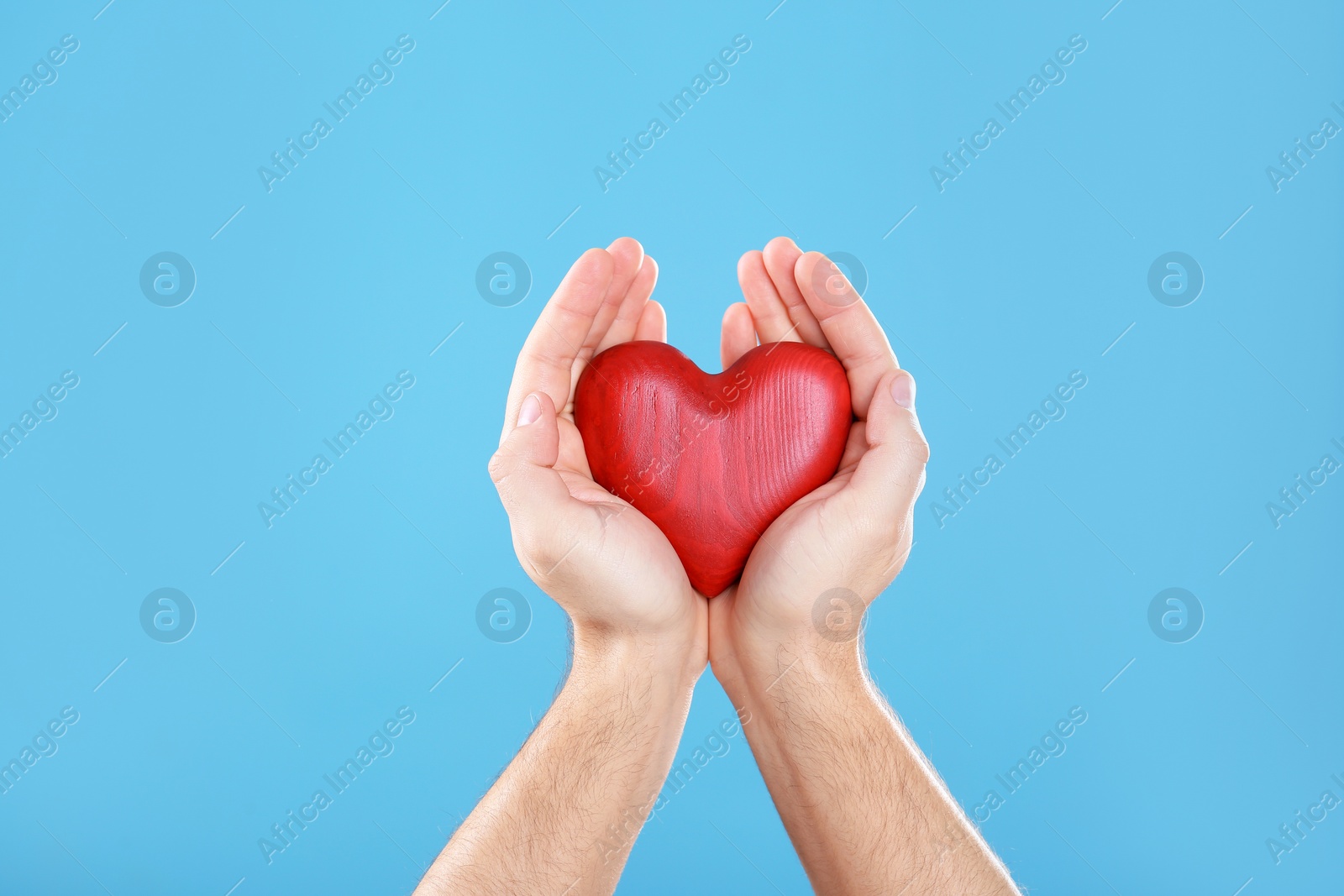 Photo of Man holding decorative heart in hands on color background, closeup