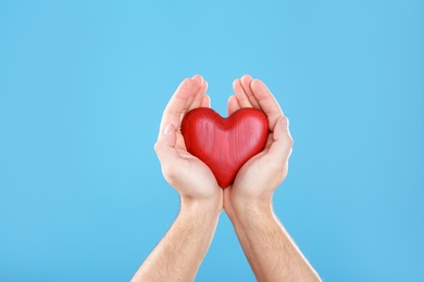 Photo of Man holding decorative heart in hands on color background, closeup