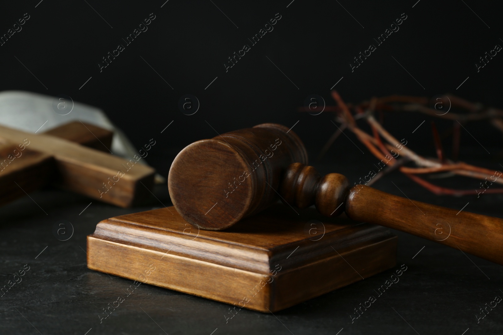 Photo of Wooden judge gavel and crown of thorns on black table, closeup