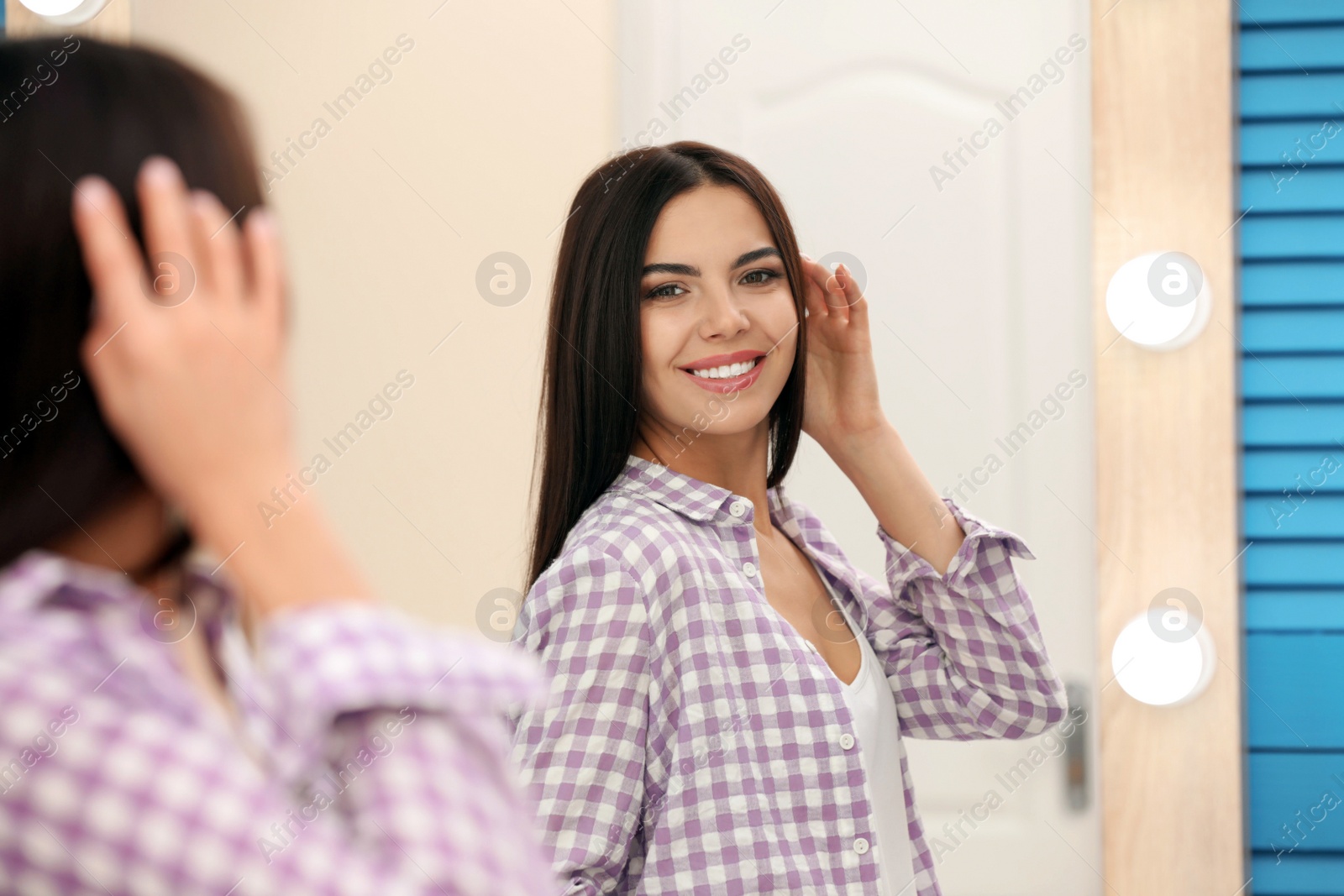 Photo of Young attractive woman looking at herself in stylish mirror at home