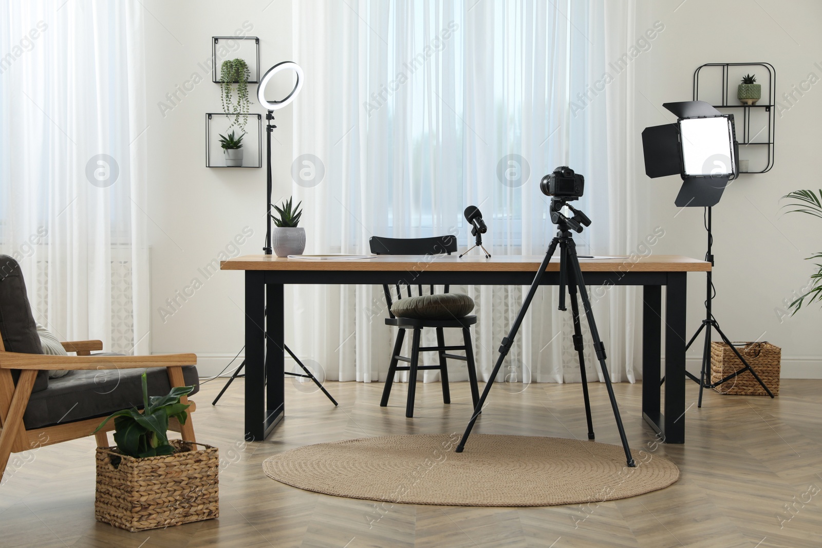 Photo of Camera and lighting equipment on tripods near table in room. Blogger workplace