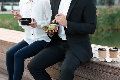 Business people eating from lunch boxes outdoors, closeup