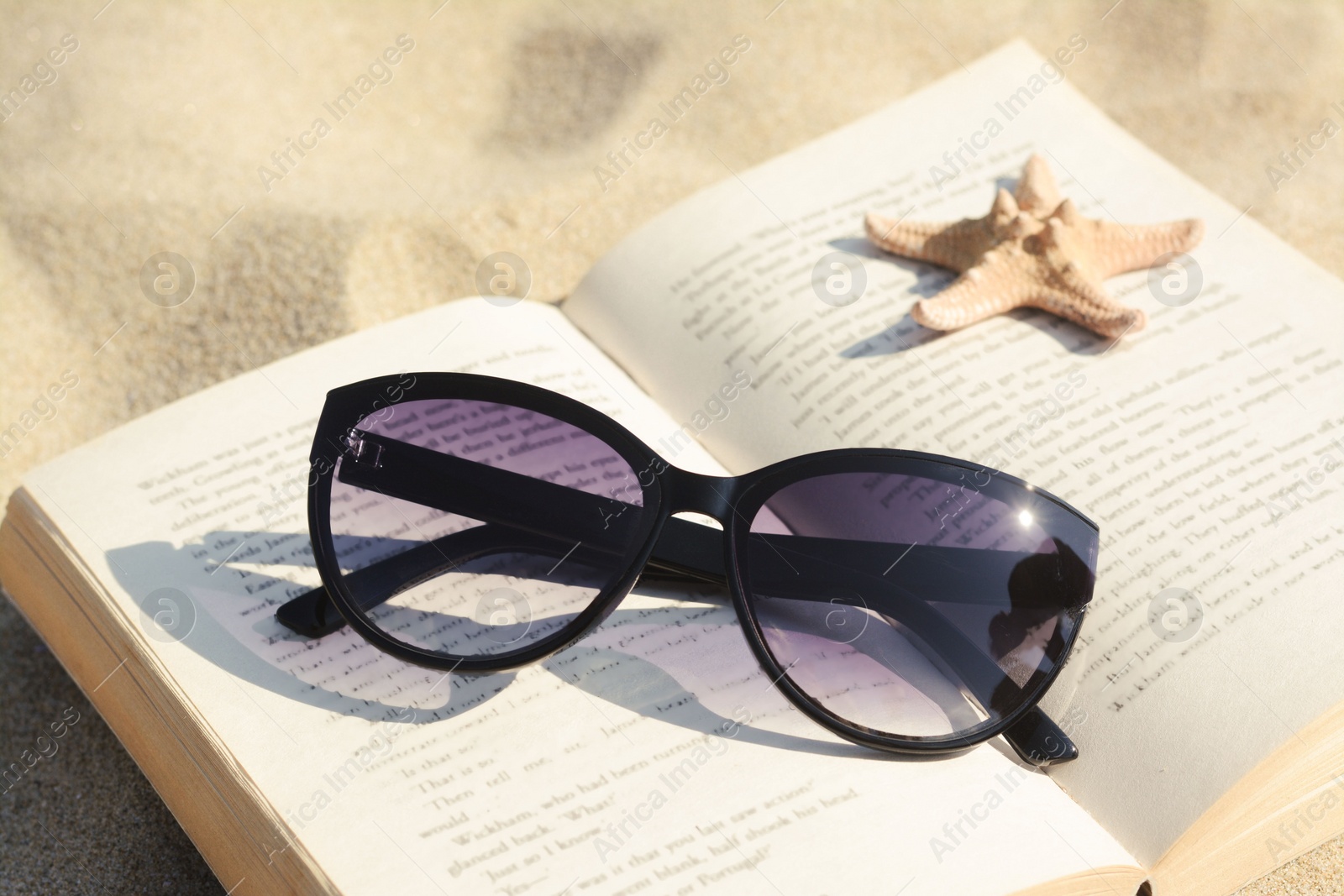 Photo of Beautiful sunglasses, book and starfish on sand, closeup