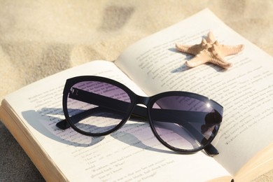 Beautiful sunglasses, book and starfish on sand, closeup