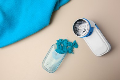 Photo of Disassembled fabric shaver with lint and light blue cloth on beige background, flat lay