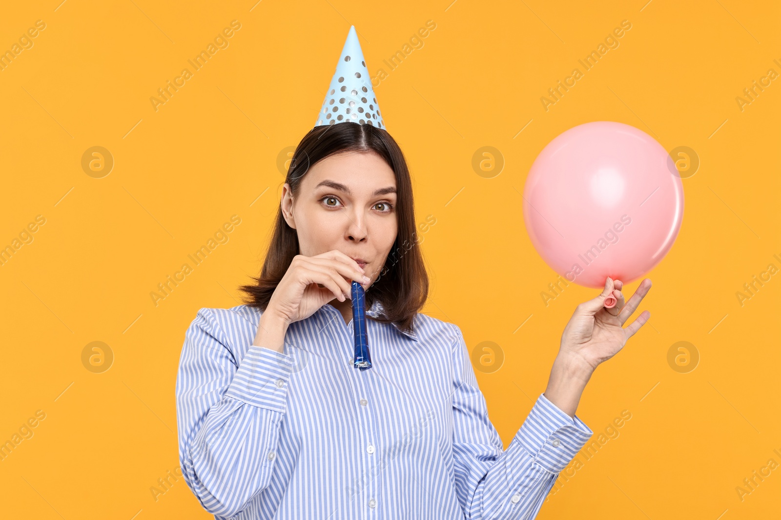 Photo of Young woman in party hat with balloon and blower on yellow background