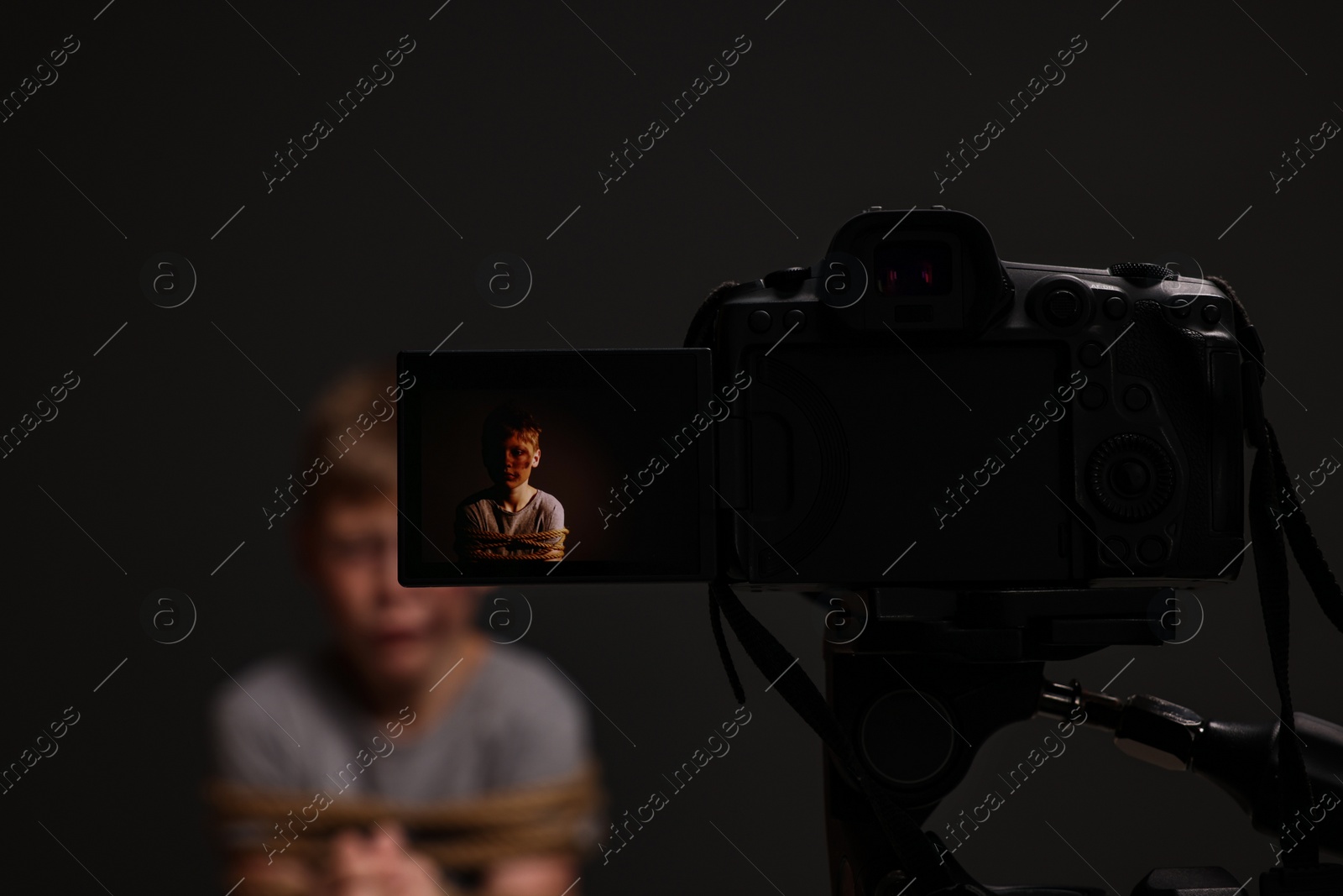 Photo of Little boy with bruises tied up and taken hostage on dark background, view through camera screen