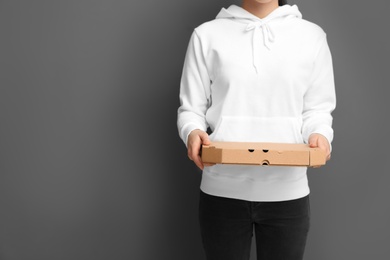 Photo of Young woman with pizza box on grey background, space for text. Food delivery service