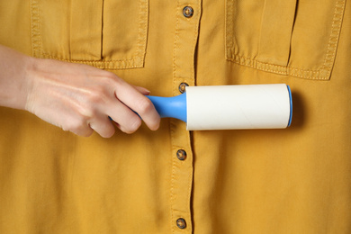 Woman cleaning yellow shirt with lint roller, closeup