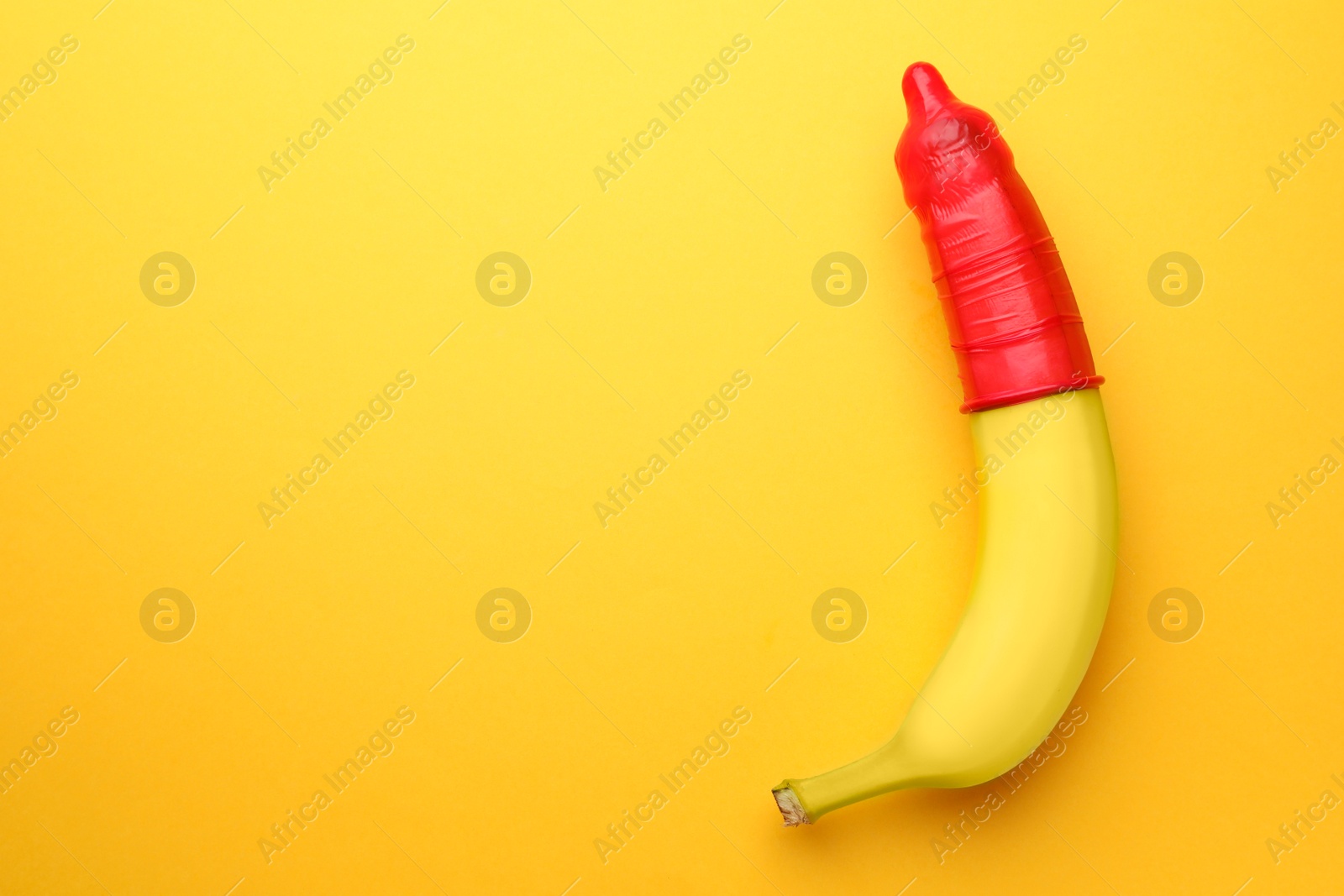 Photo of Banana with condom on orange background, top view and space for text. Safe sex concept