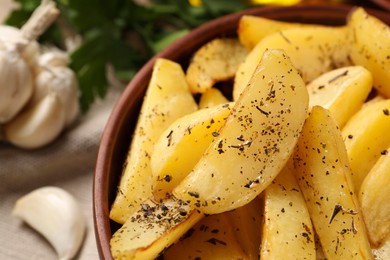 Photo of Bowl with tasty baked potato wedges and spices on table, closeup