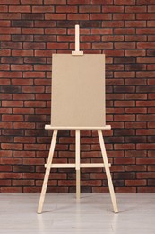 Wooden easel with blank board near brick wall indoors