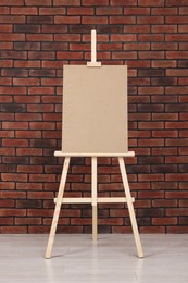 Photo of Wooden easel with blank board near brick wall indoors