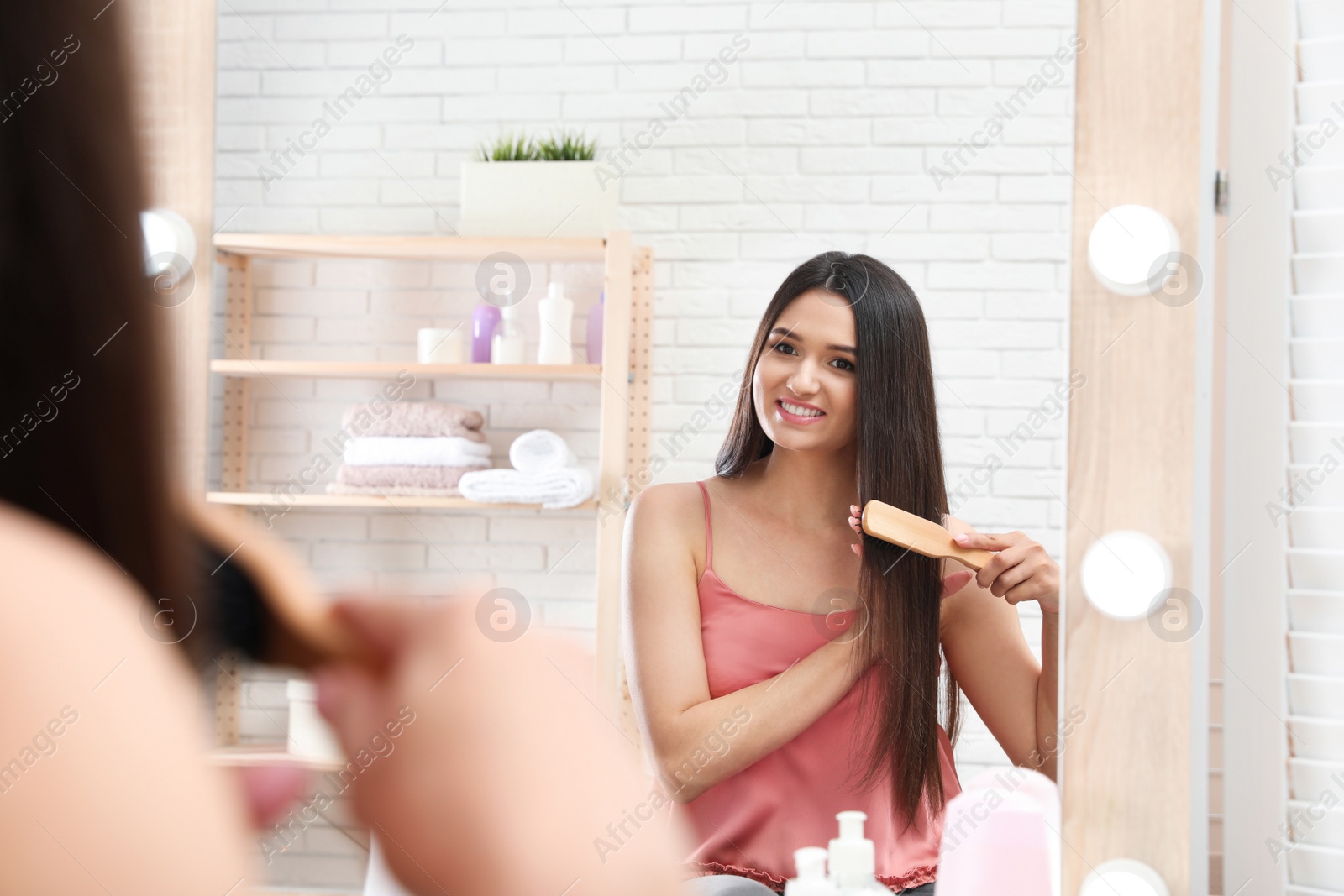 Photo of Beautiful young woman with hair brush looking into mirror in bathroom