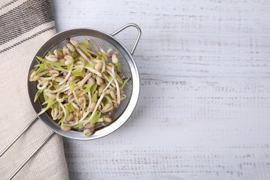 Photo of Mung bean sprouts in strainer and kitchen towel on white wooden table, top view. Space for text