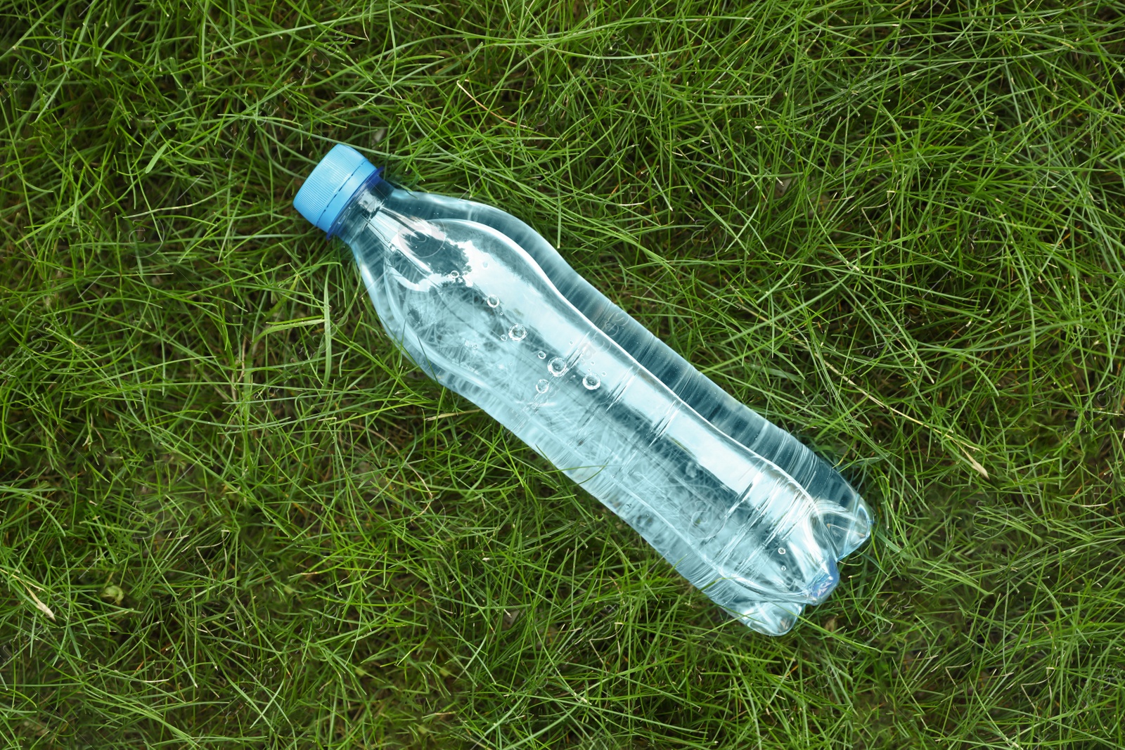 Photo of Bottle of fresh water on green grass, top view