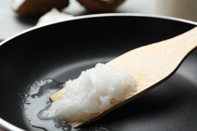 Photo of Frying pan with coconut oil and wooden spatula, closeup. Healthy cooking