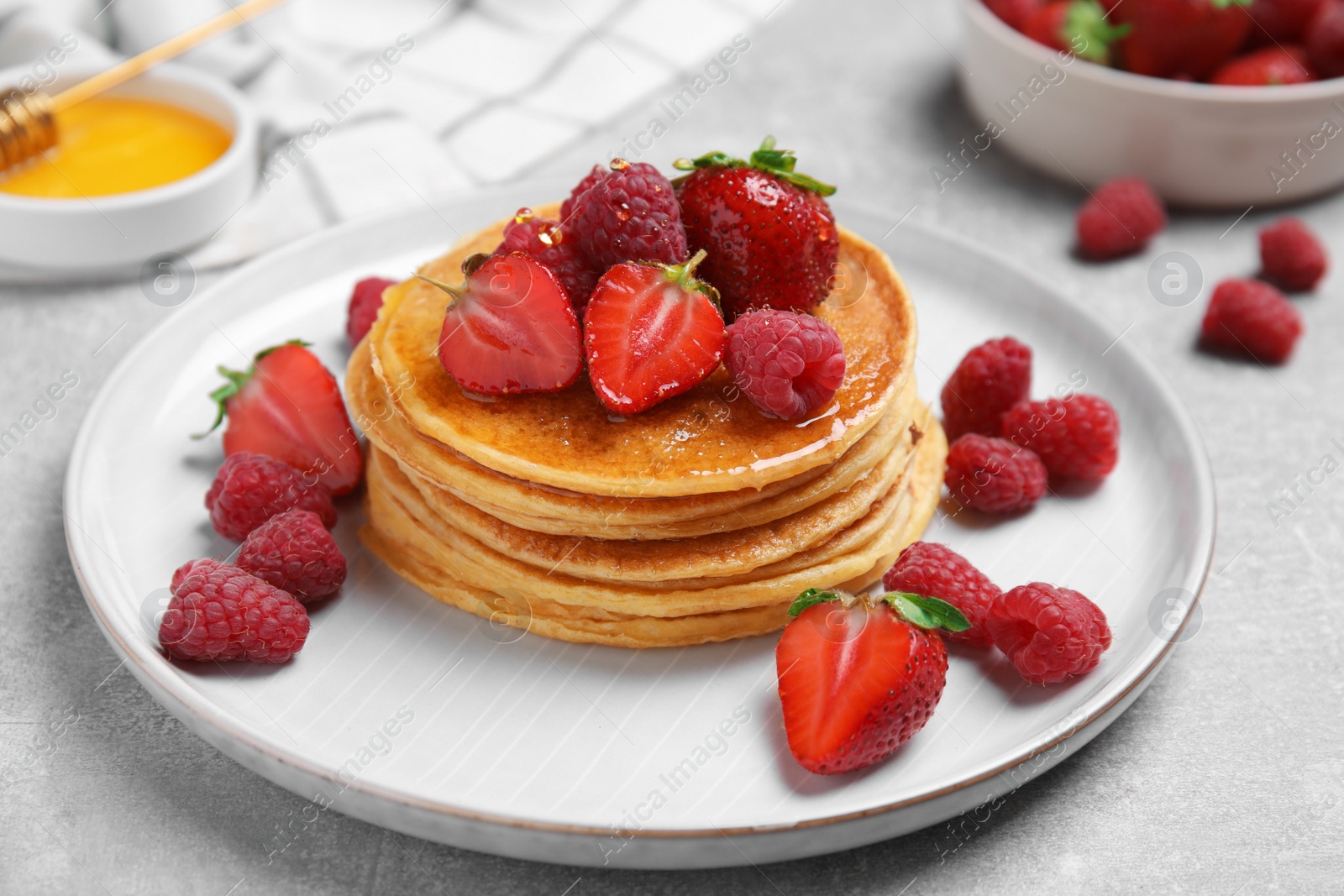 Photo of Tasty pancakes with fresh berries and honey on light grey table, closeup