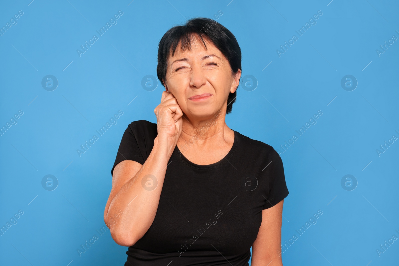 Photo of Senior woman suffering from ear pain on light blue background