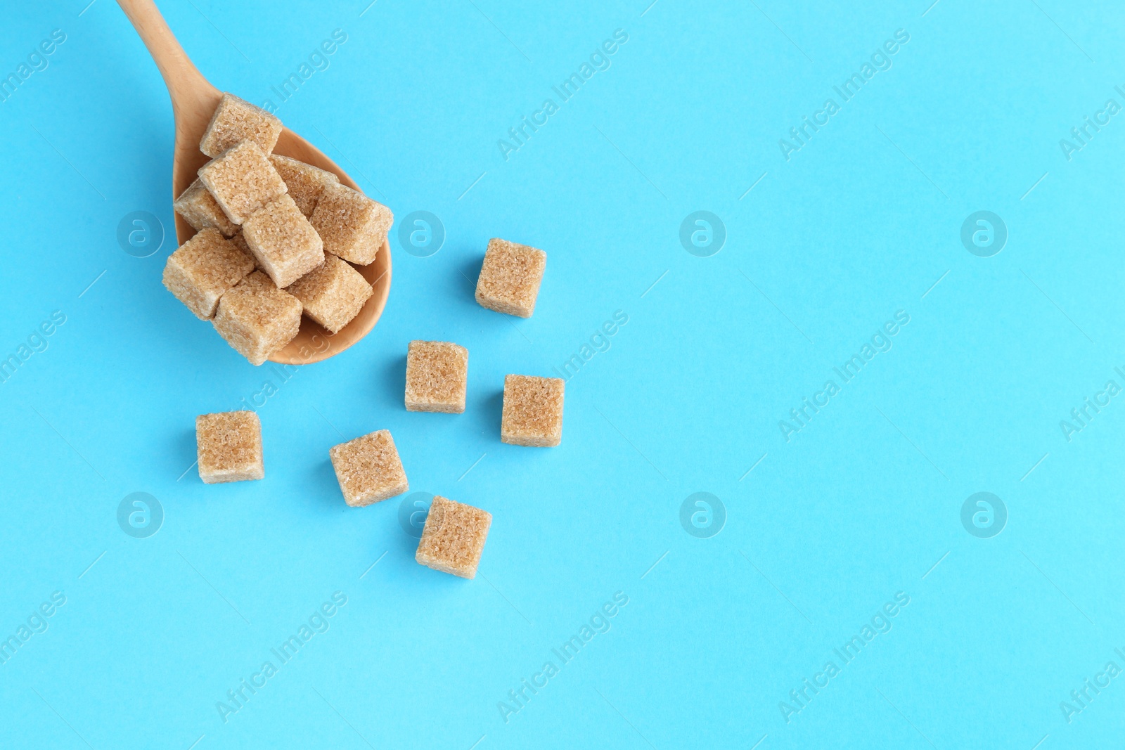 Photo of Brown sugar cubes and spoon on light blue background, top view. Space for text