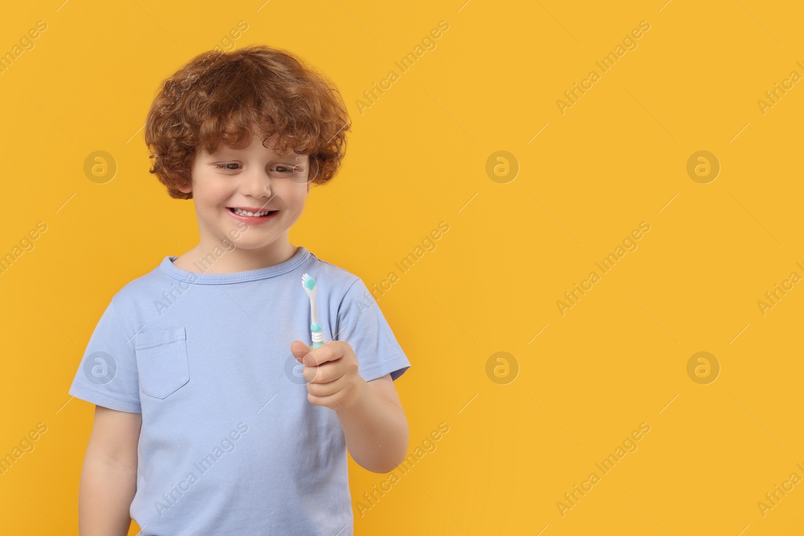 Photo of Cute little boy holding plastic toothbrush on yellow background, space for text