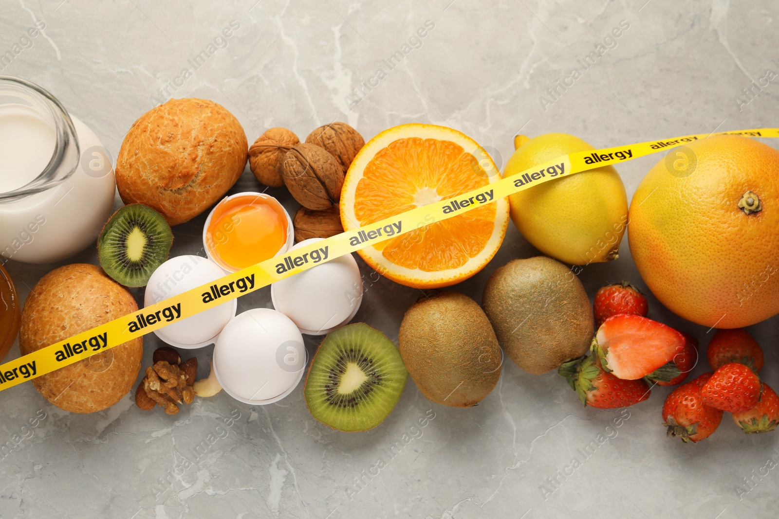 Photo of Allergenic food. Different fresh products with tape on gray marble table, top view