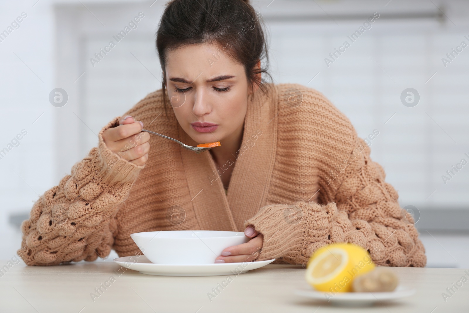 Photo of Sick young woman eating soup to cure flu at table in kitchen