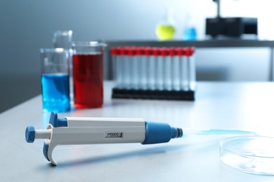 Photo of Laboratory analysis. Micropipette, petri dish, beakers with liquids and test tubes on grey table