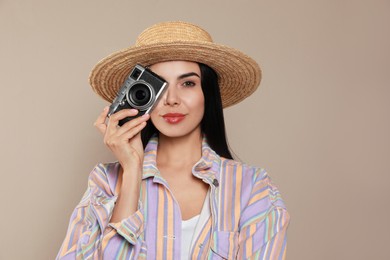 Beautiful young woman with straw hat and camera on beige background