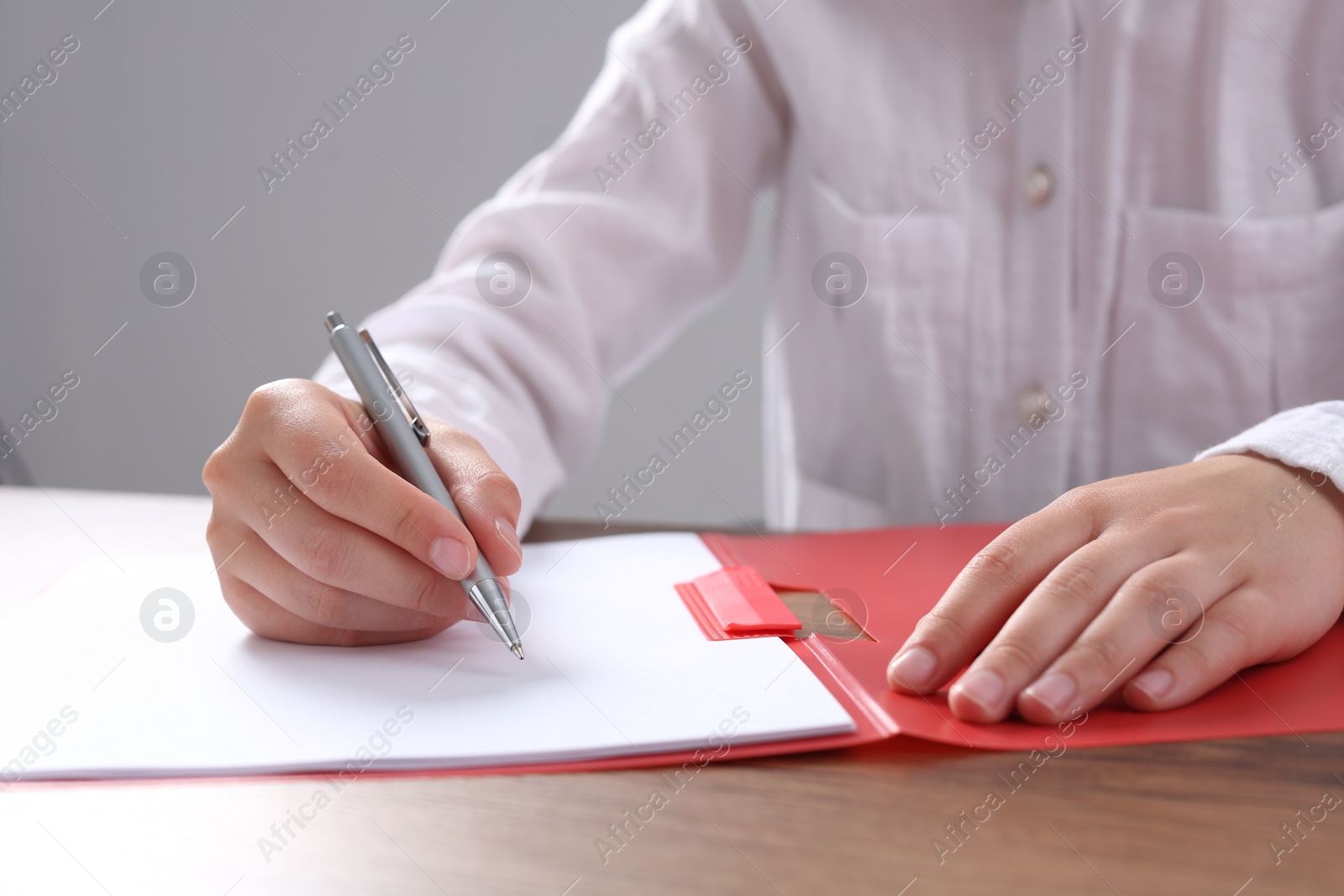 Photo of Woman writing on sheet of paper in red folder at wooden table in office, closeup