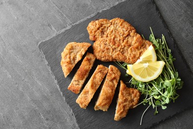 Photo of Tasty schnitzels served with microgreens and lemon on grey table, top view