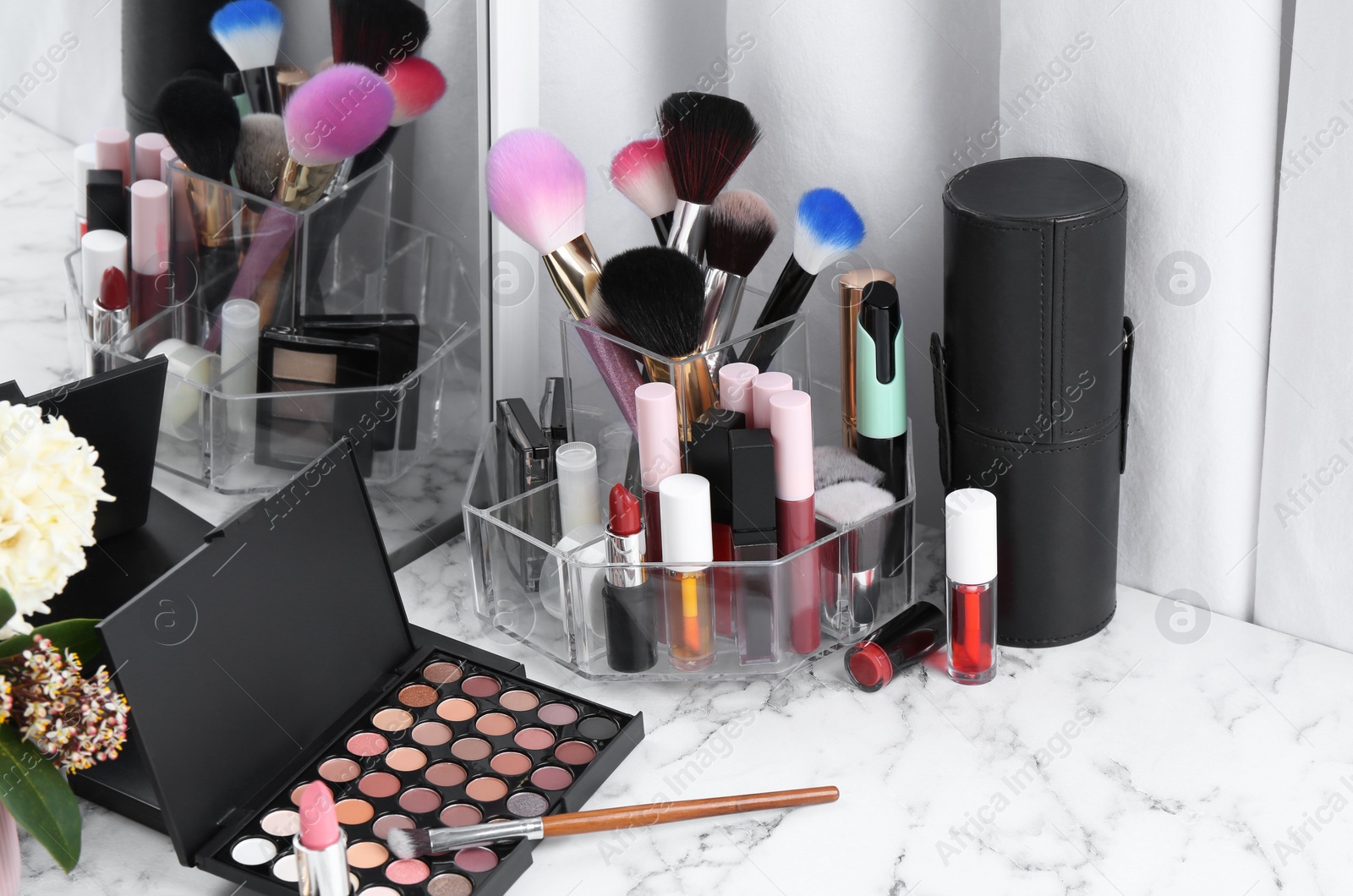 Photo of Bright lip glosses among different cosmetic products on white dressing table