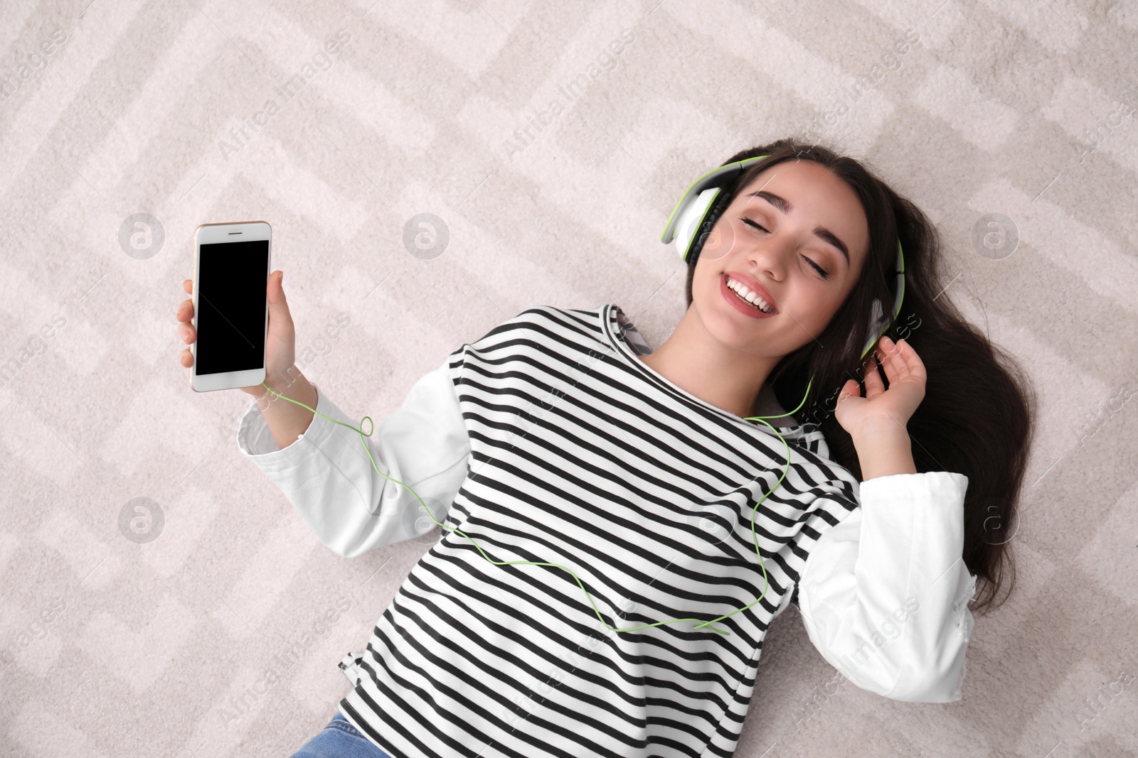 Photo of Young woman in headphones with mobile device enjoying music on floor, top view. Space for text