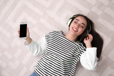 Photo of Young woman in headphones with mobile device enjoying music on floor, top view. Space for text