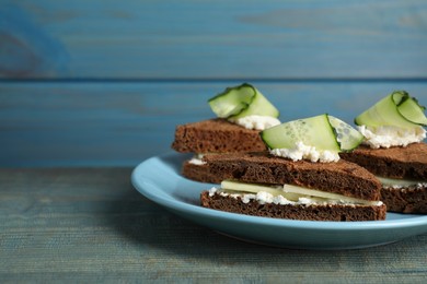 Photo of Plate of tasty sandwiches with cucumber and cream cheese on light blue wooden table. Space for text