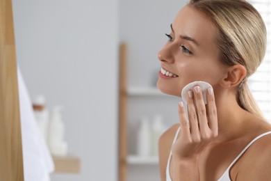 Photo of Smiling woman removing makeup with cotton pad indoors. Space for text