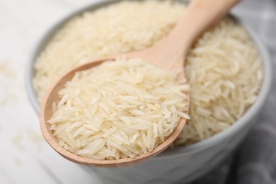 Wooden spoon and bowl with raw rice on table, closeup