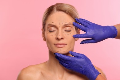 Photo of Doctor checking patient's face before cosmetic surgery operation on pink background