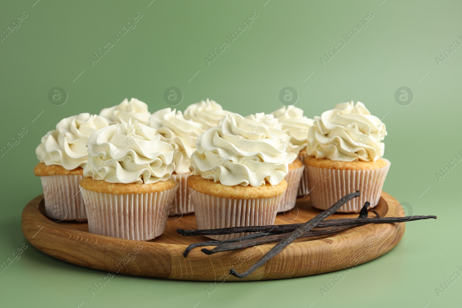 Photo of Tasty cupcakes with cream and vanilla pods on green background