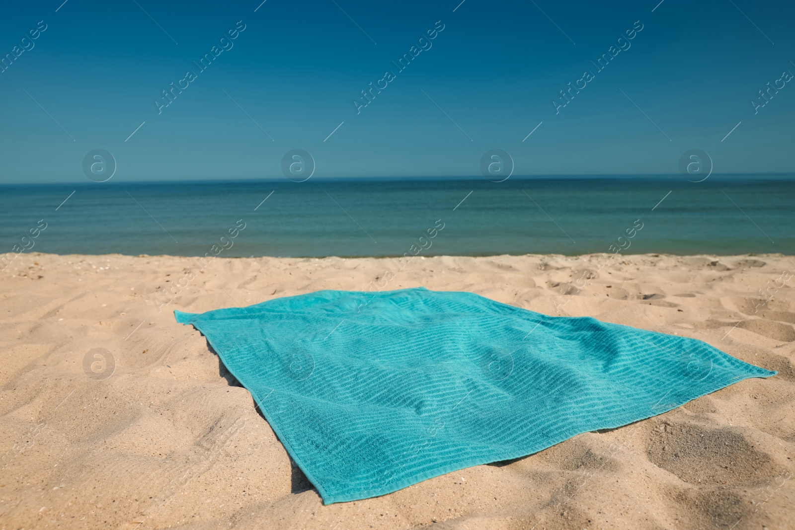 Photo of Turquoise beach towel on sand near sea, space for text