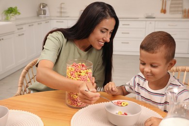 Photo of Happy mother feeding her son at table in kitchen