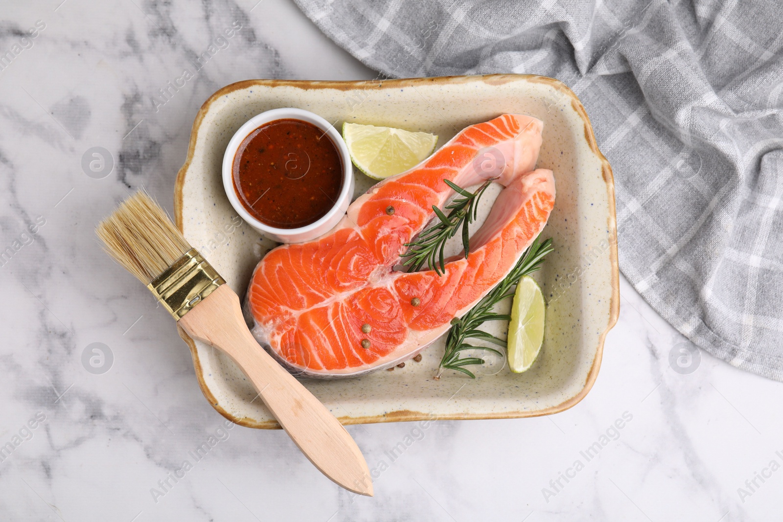 Photo of Fresh fish, lime, rosemary and marinade in baking dish on light marble table, top view