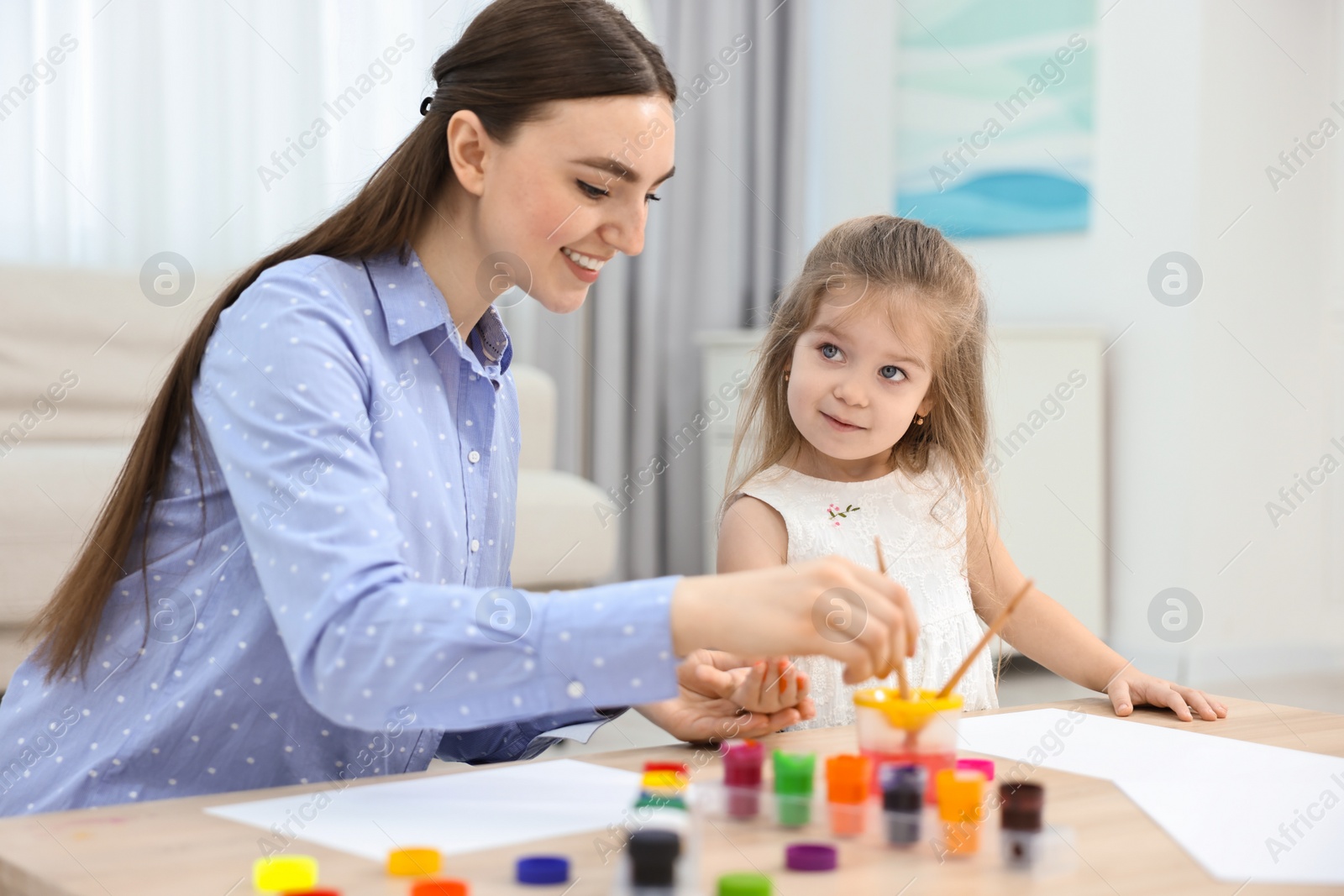 Photo of Mother and her little daughter painting with palms at home