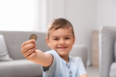Cute little boy holding coin at home, focus on hand