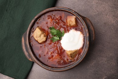 Photo of Tasty borscht with sour cream in bowl on brown textured table, top view
