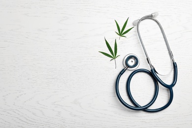 Photo of Hemp leaves and stethoscope on white wooden background, flat lay. Space for text