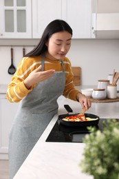 Photo of Beautiful woman cooking and smelling vegetable dish in kitchen