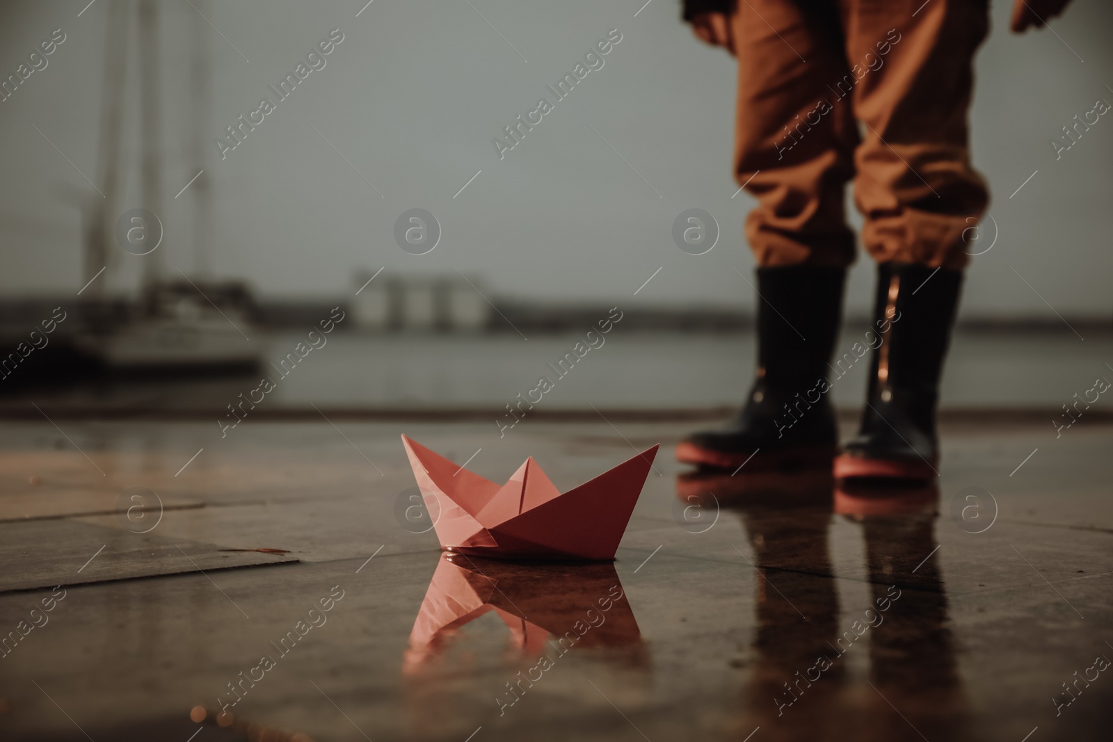 Photo of Little boy outdoors, focus on paper boat in puddle