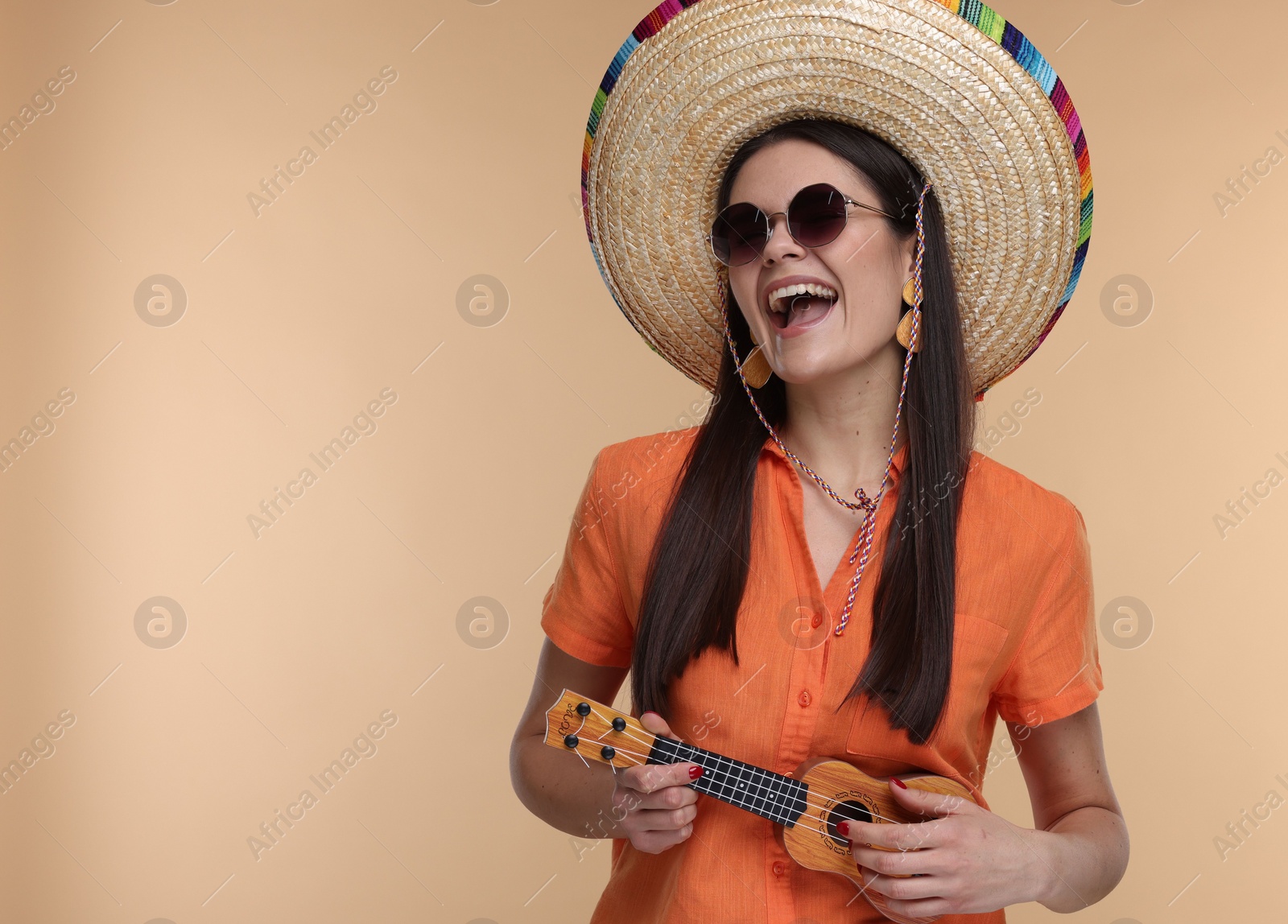 Photo of Young woman in Mexican sombrero hat playing ukulele on beige background. Space for text