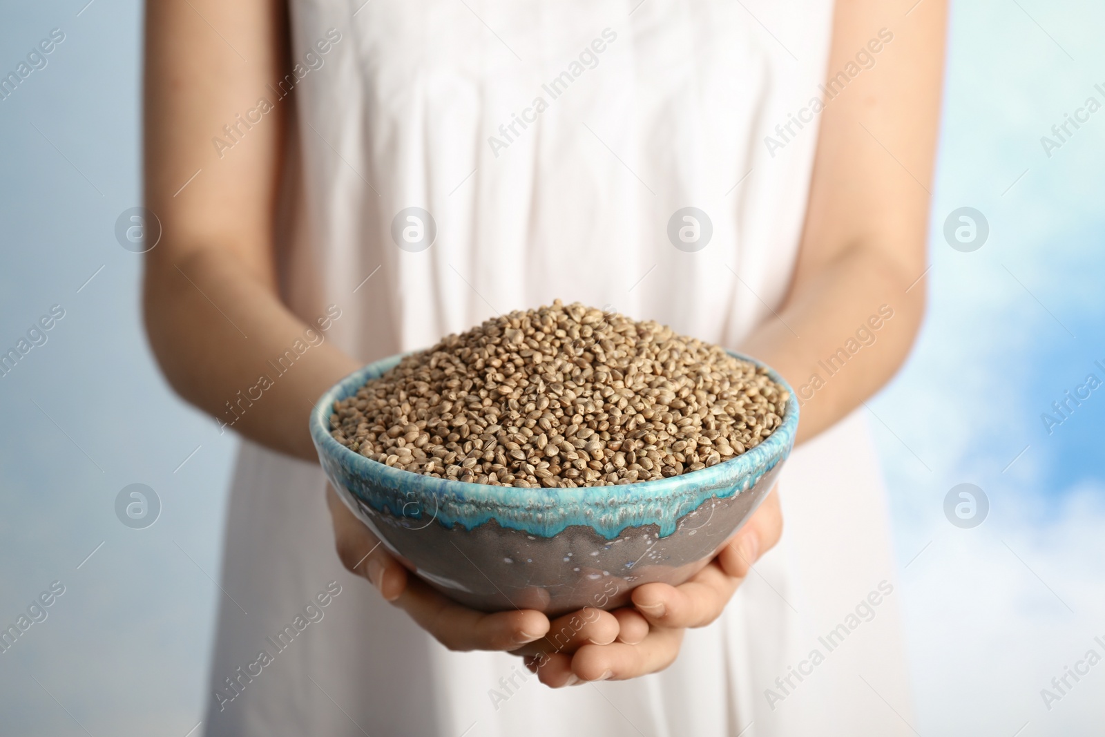 Photo of Woman holding bowl with hemp seeds on color background, closeup